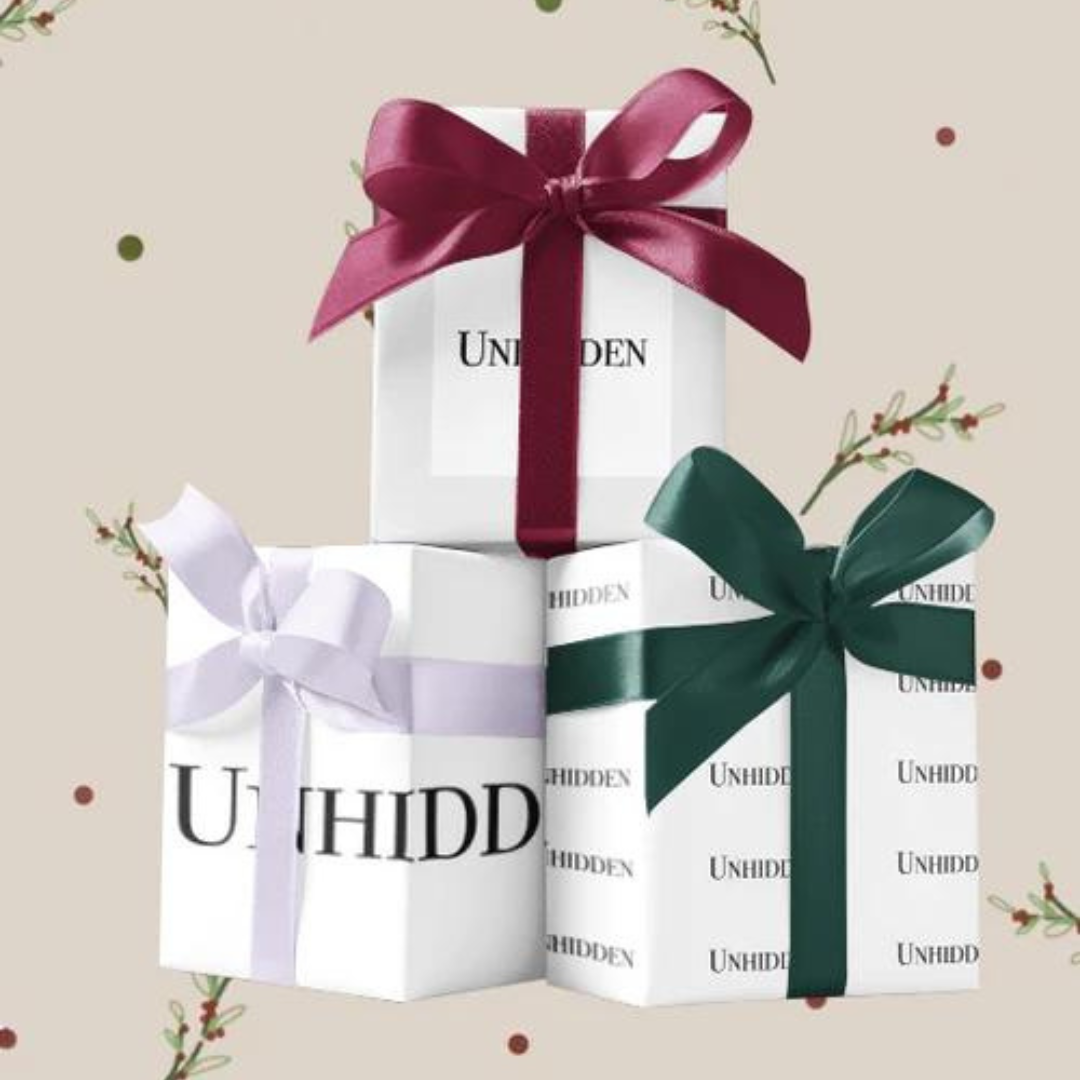 Three boxes are stacked with two at the bottom. One on the left has a pale lilac ribbon, middle has a burgundy and the right one has a forest green ribbon. The background is beige with Christmas motifs.