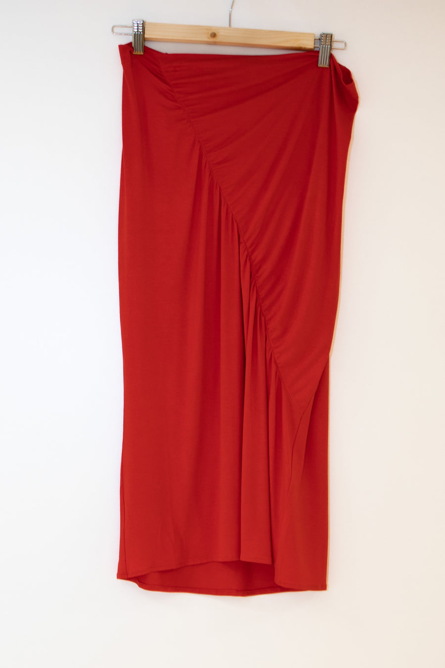 Ruched skirt in coral hanging on a wooden clip hanger against a white background