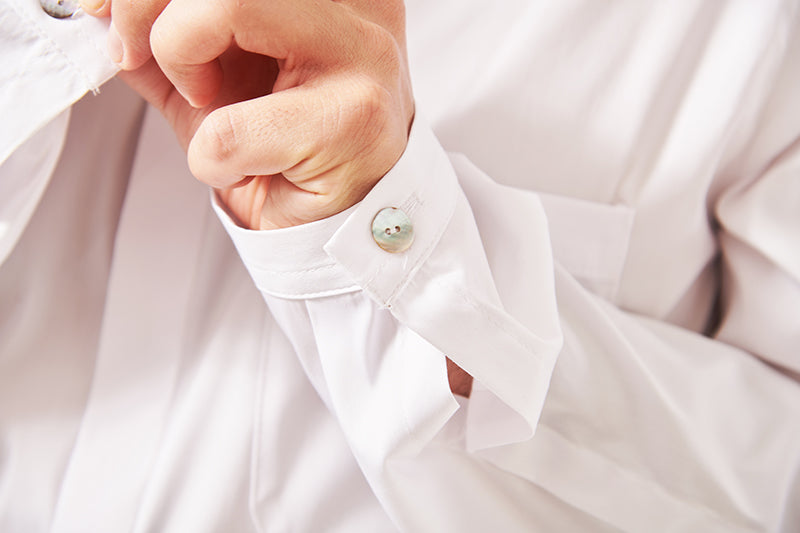 Close up shot of a mans' shirt cuff. There is a shell button. The shirt is white.