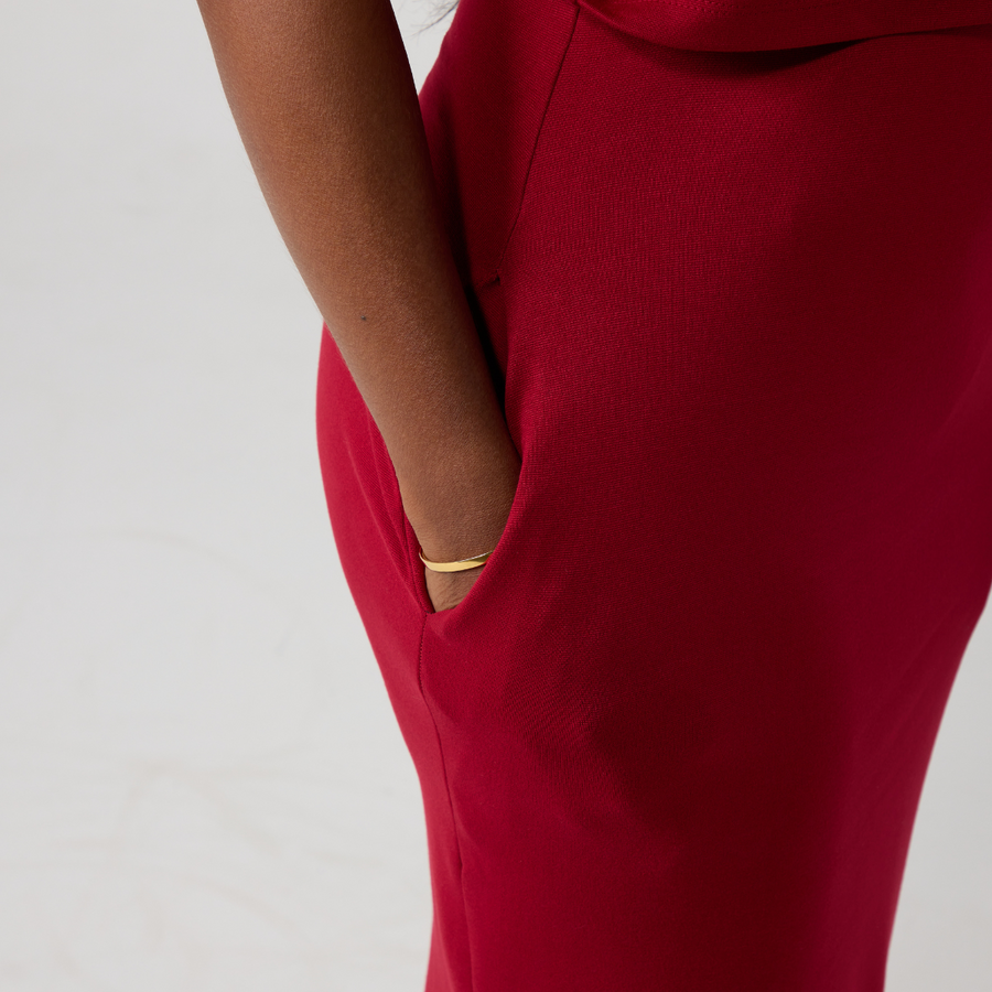 Close up of a raspberry red dress with a south asian womans' hand in the pocket. She has a gold bangle visible as well.