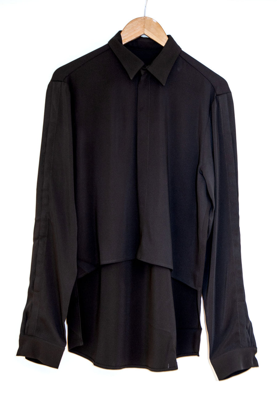 Black lyocell shirt on a wooden hanger against white background. Concealed front fastening and sleeve opening.