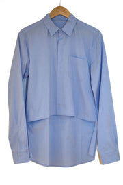 Pale blue cotton shirt on a wooden hanger against white background. There is a chest pocket on the left side as worn. Concealed front fastening and sleeve opening.