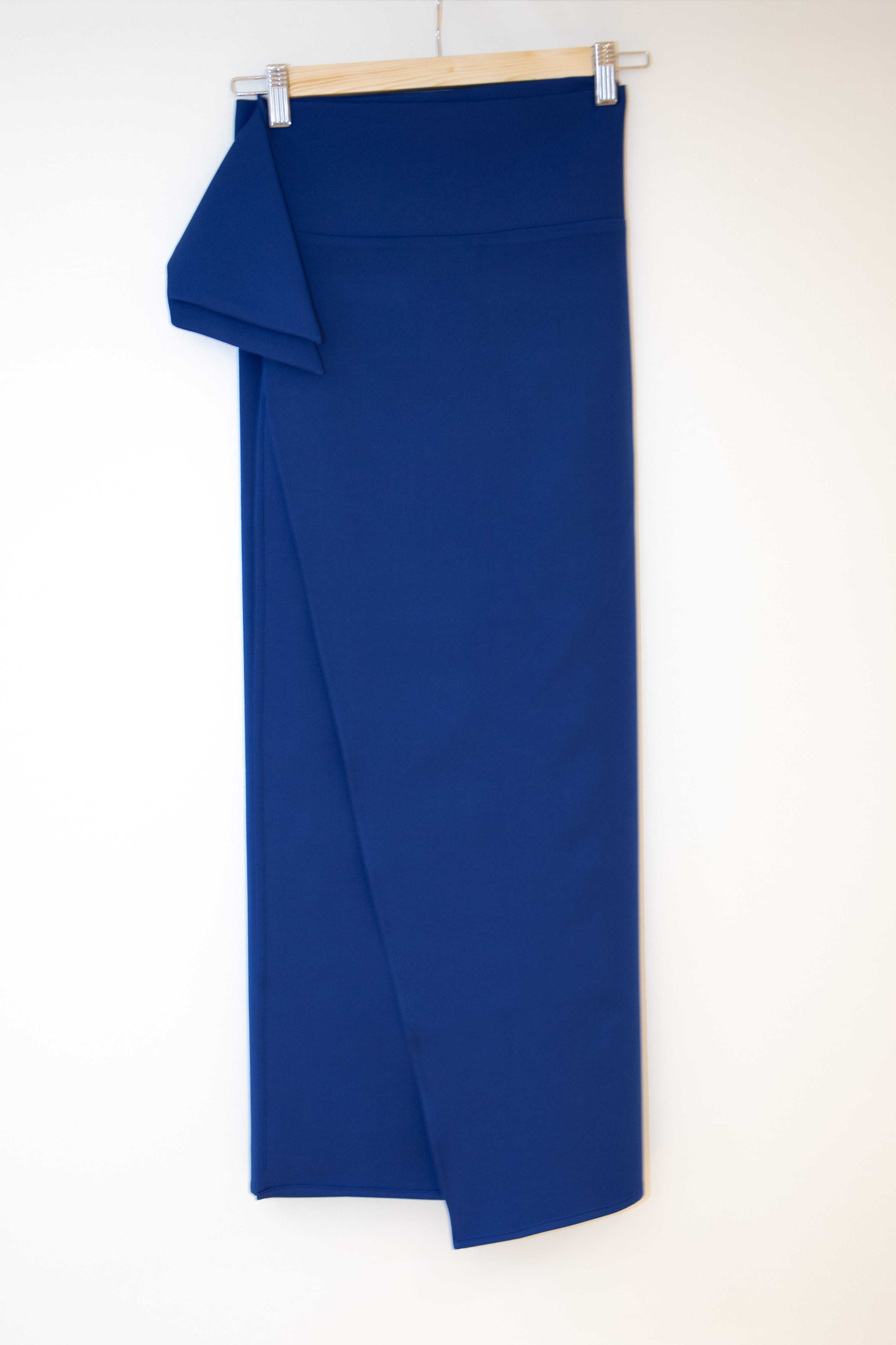 Cobalt blue wrap skirt on a wooden clip hanger on a white background