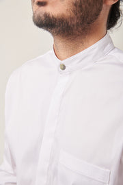 A close up of the neck and chest of a south Asian man wearing a white shirt with a mandarin collar and shell button. He has a short beard and his hair is tied up.